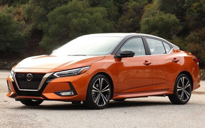 Sedã Nissan Sentra laranja estacionado em estrada com vegetação ao fundo